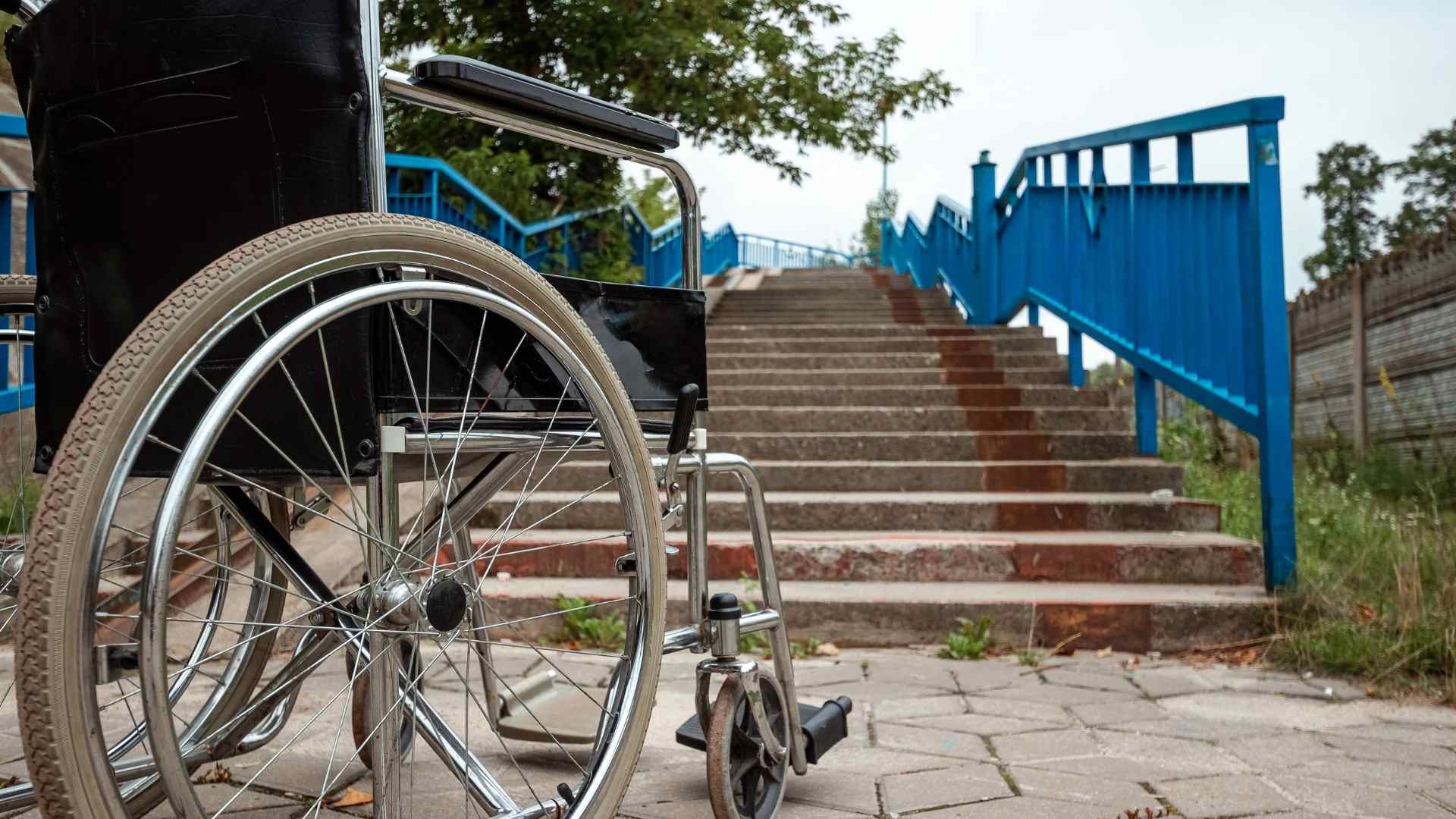 כיסא גלגלים עומד למרגלות מדרגות ללא רמפה נגישה – המחשה לחשיבות יישום חוק נגישות לנכים במרחב הציבורי.